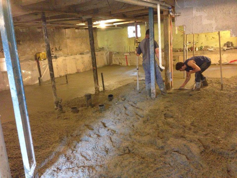 Deux hommes travaillent sur un sol en béton dans un sous-sol.