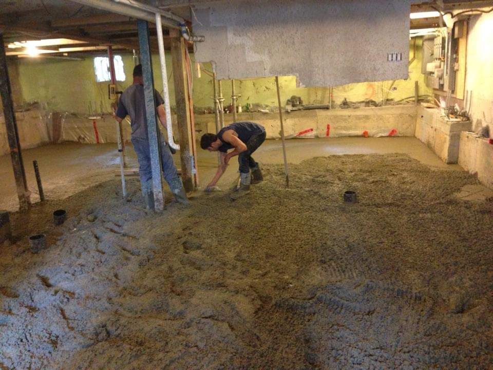 Deux hommes travaillent sur un sol en béton dans un sous-sol