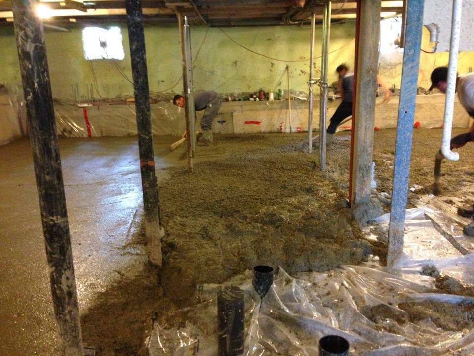 Un homme pose du béton dans un sous-sol.