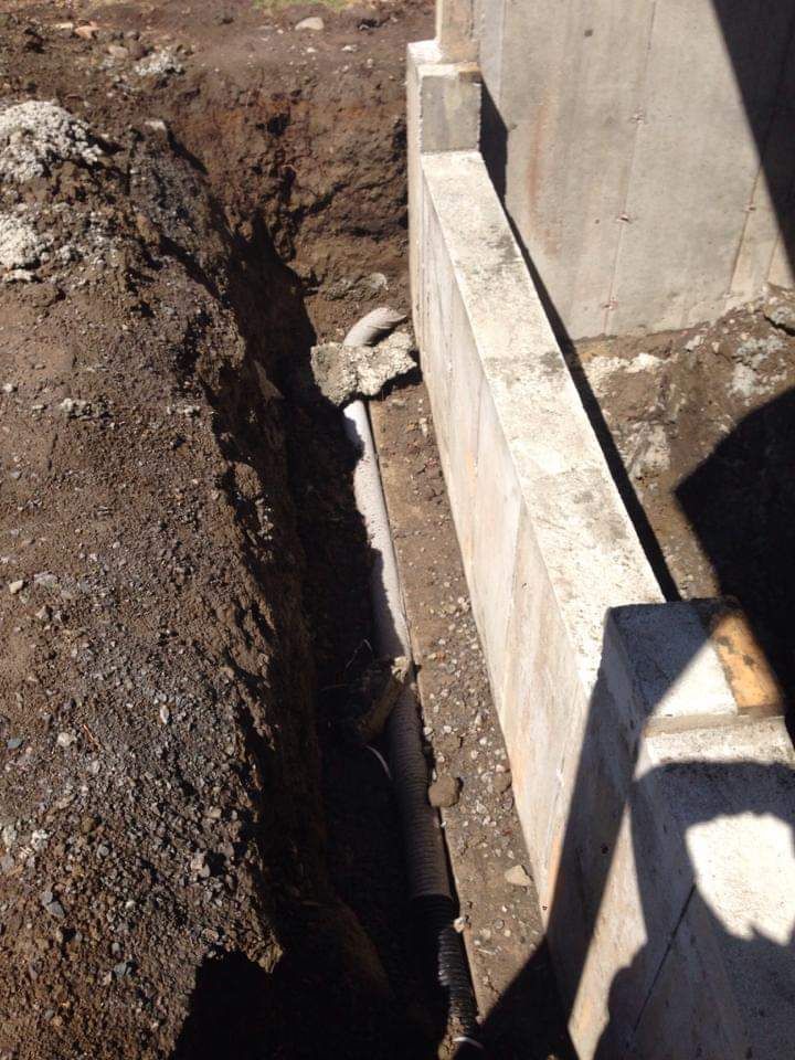 Une personne creuse un trou dans le sol à côté d'un mur de béton.