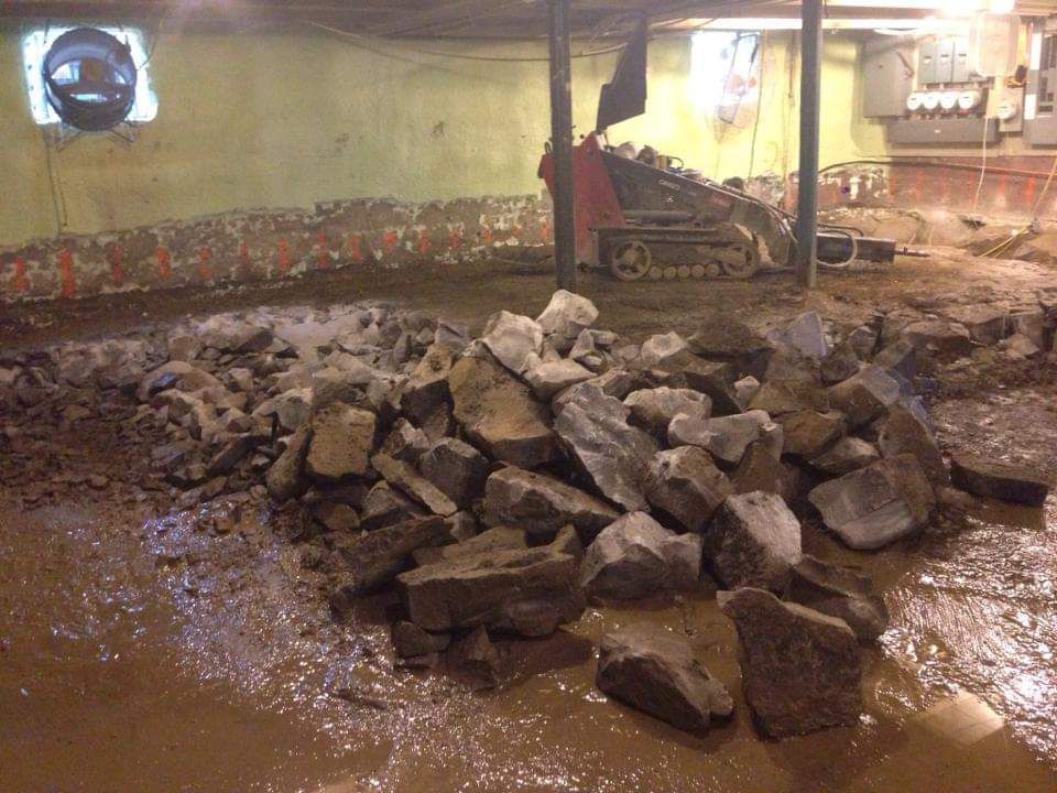 Un tas de roches dans un sous-sol inondé avec un bulldozer en arrière-plan.