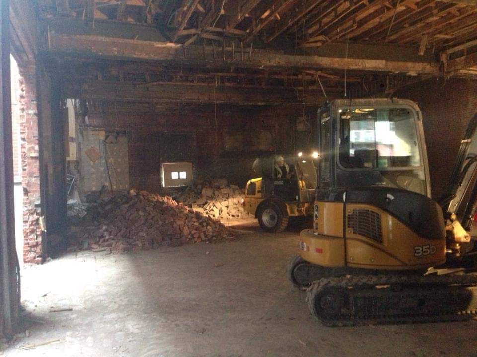 Une petite excavatrice se trouve dans un bâtiment vide à côté d'un chariot élévateur.