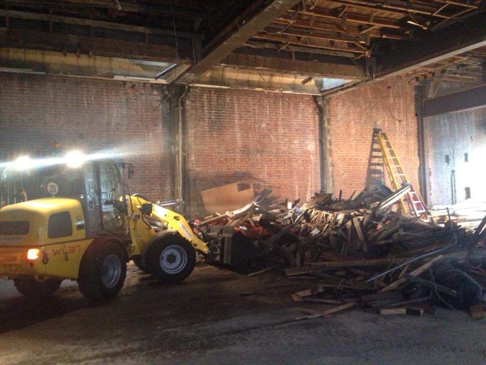 Un tracteur jaune déplace un tas de bois dans un entrepôt.