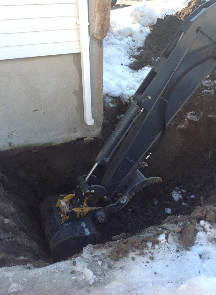 Une excavatrice creuse un trou dans le sol devant une maison.