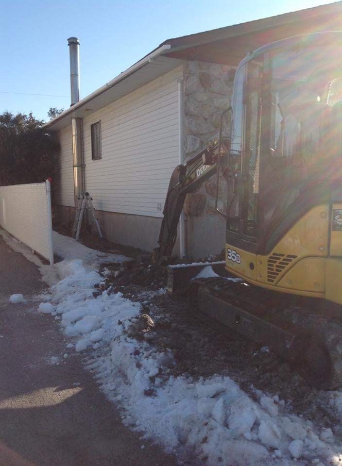Une excavatrice jaune creuse un trou devant une maison.