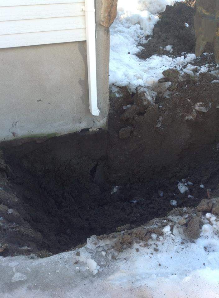 Un trou dans le sol à côté d'une maison avec de la neige au sol.