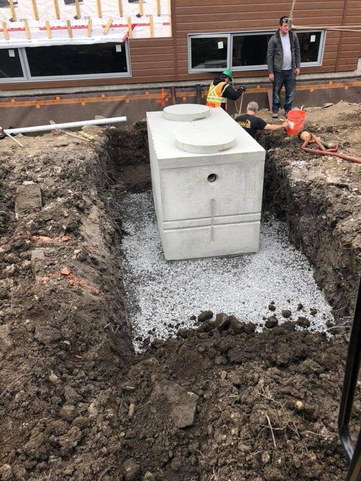 Une fosse septique en béton est en cours d'installation dans un trou dans le sol.