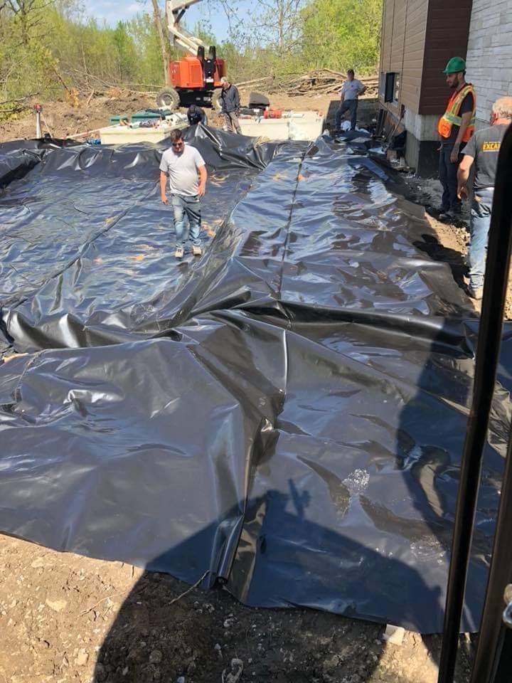Un groupe d'ouvriers du bâtiment se tient debout sur un gros morceau de plastique noir.