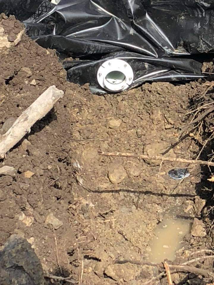 Un tuyau blanc est posé dans la terre à côté d'un sac en plastique noir.
