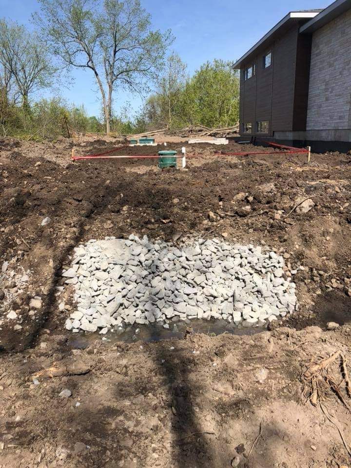 Un gros tas de gravier se trouve au milieu d'un champ de terre devant une maison.