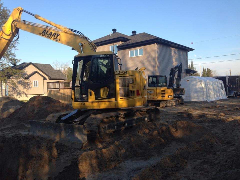 Une excavatrice jaune creuse un trou devant une maison.