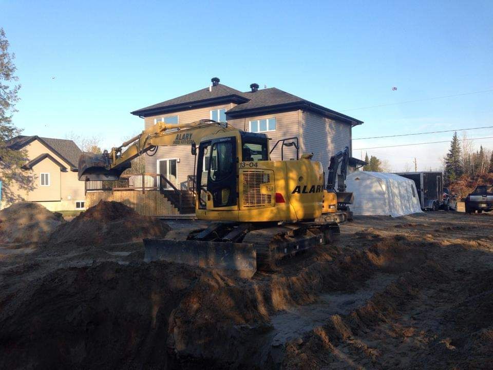 Une excavatrice jaune creuse un trou devant une maison.