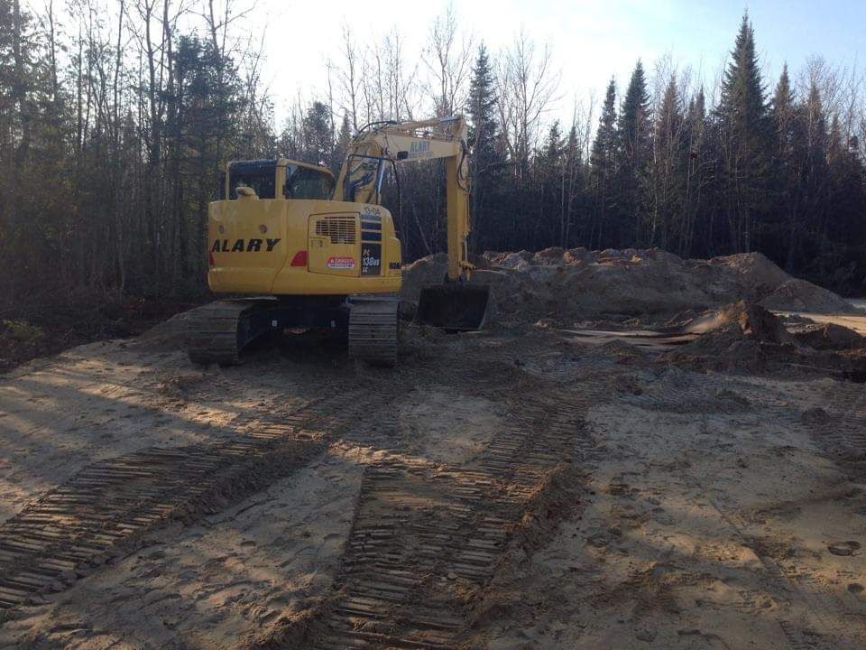 Une excavatrice jaune est assise au milieu d'un chemin de terre.