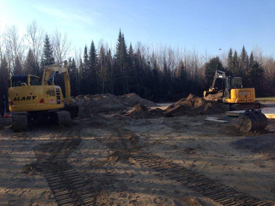 Deux bulldozers sont assis dans un champ de terre avec des arbres en arrière-plan.