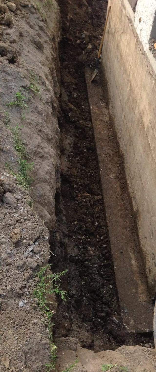 Une personne creuse un trou dans le sol à côté d'un mur de béton.