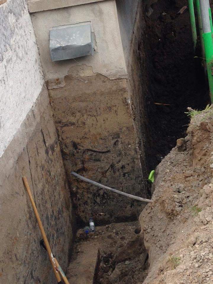 Une personne creuse un trou dans le sol à côté d'un mur.