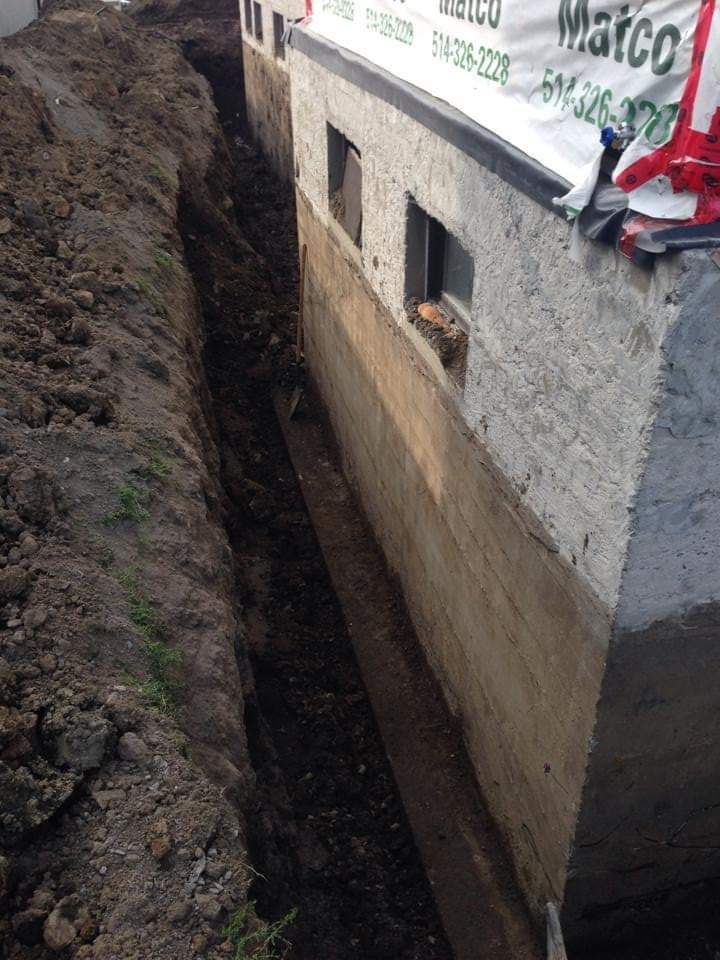 Un système de drainage est en cours d'installation sur le côté d'un bâtiment.
