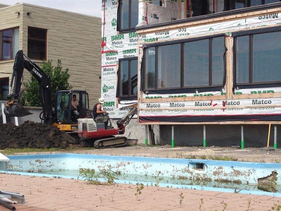 Une excavatrice déplace de la terre devant un bâtiment qui dit marco