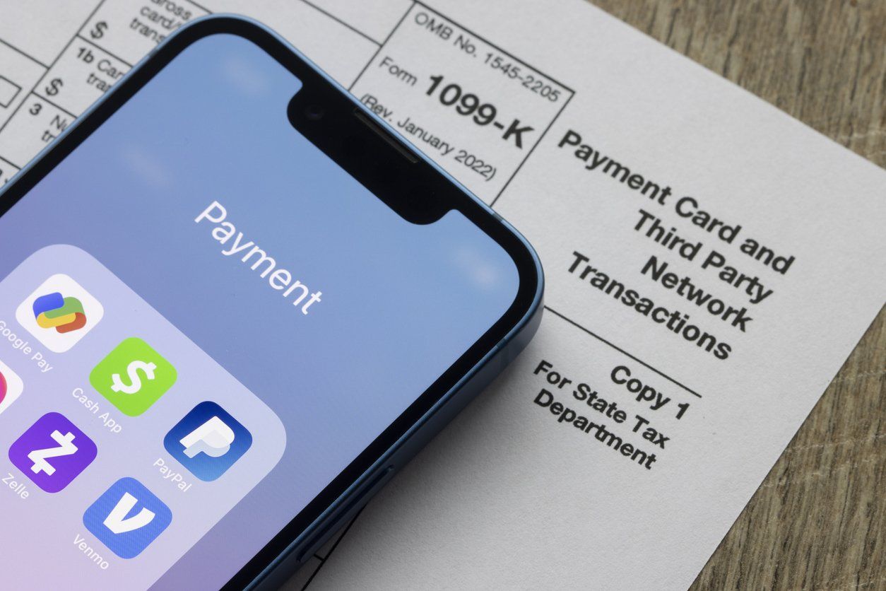 Smartphone showing third-party payment apps like Venmo on top of a 1099-K form - Venmo reporting and IRS compliance.