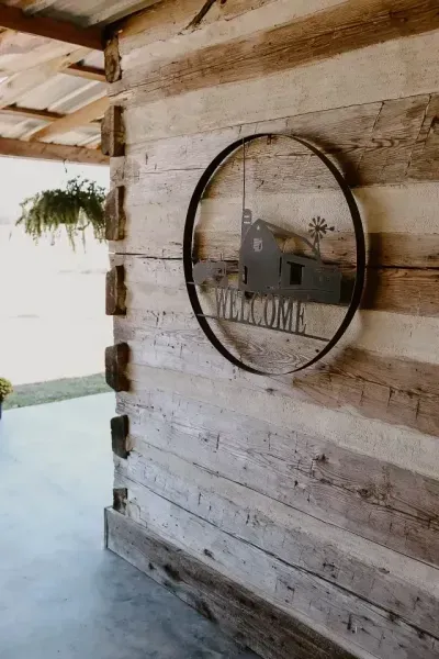 Rustic wooden wall with round metal-framed sign reading “WELCOME” on a porch entrance