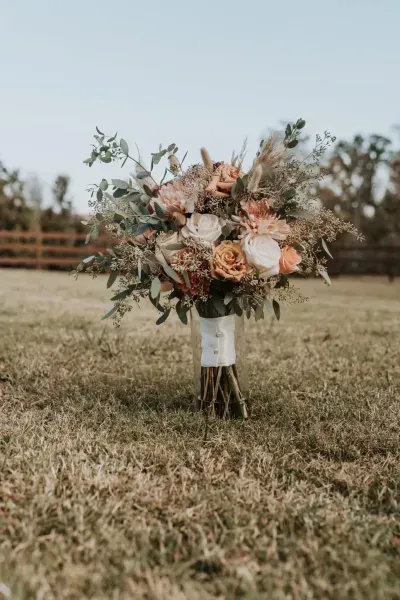 Bouquet of peach and white flowers tied to a tree stump in a grassy field.