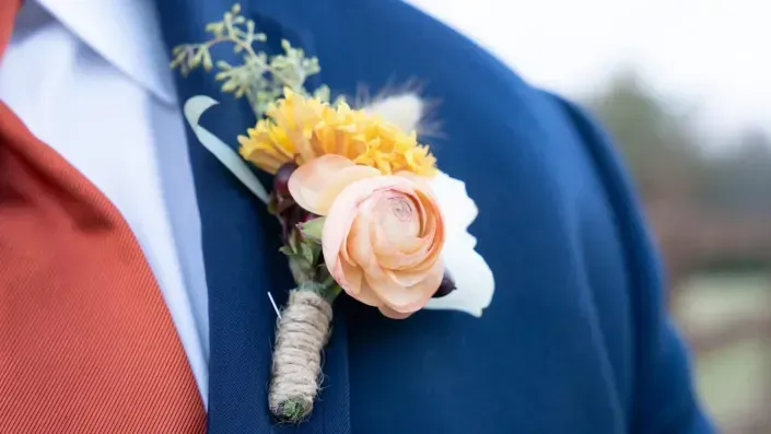 Boutonniere with peach rose and yellow flowers pinned to a navy suit jacket