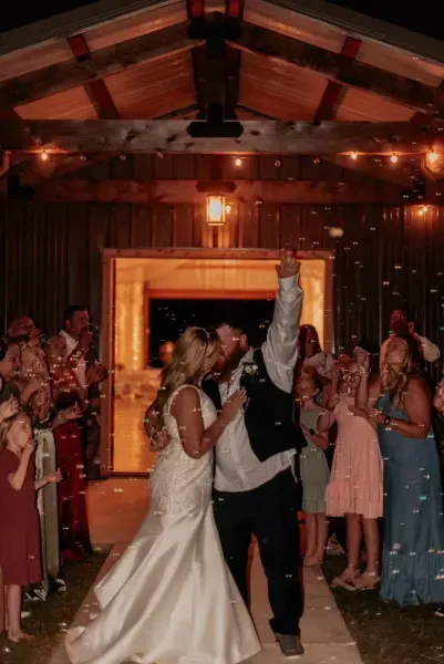 Bride and groom dance under a wooden pavilion as guests clap around them during a reception