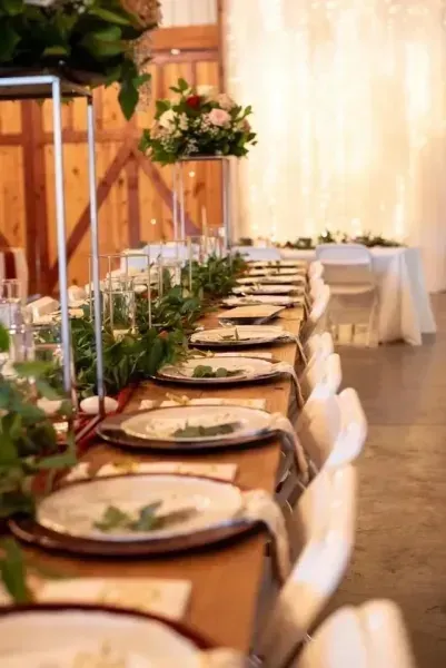 Elegant banquet table set with white chairs, floral centerpieces, and warm draped lighting in a reception hall