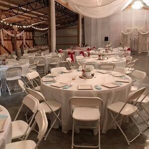 Round banquet tables and white folding chairs arranged in a decorated event hall with draped fabric.