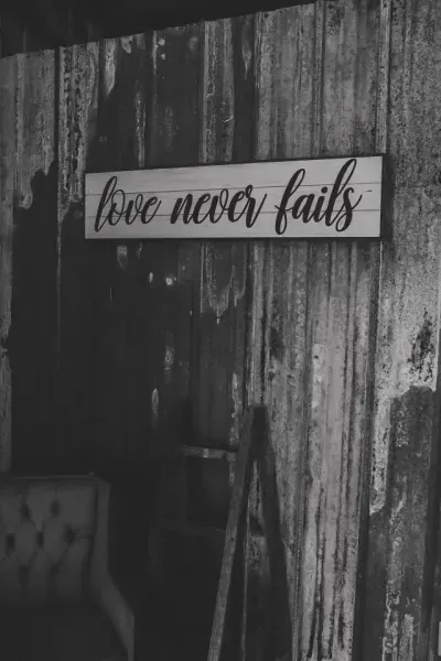 Black-and-white sign reading “love never fails” on a rustic wooden wall