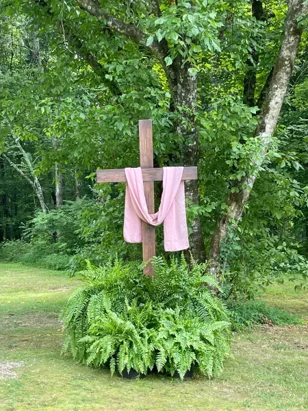 Wooden cross draped with pink cloth in a lush green garden setting