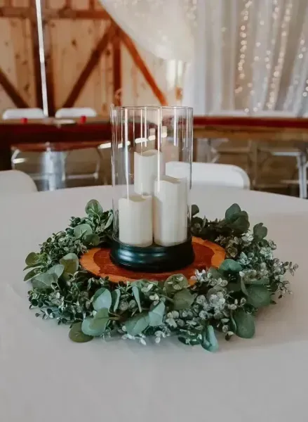 Candles in glass holders on a greenery wreath centerpiece on a white table