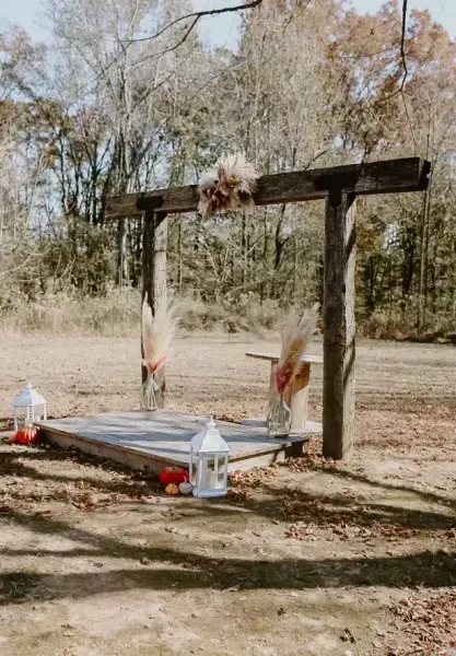 Rustic wooden wedding arch with floral decorations and lanterns on a platform in an outdoor clearing