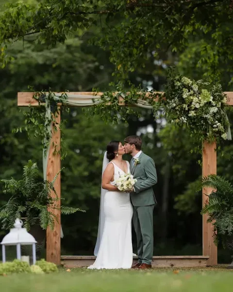 Bride and groom kissing beneath a floral wooden arch in a garden setting