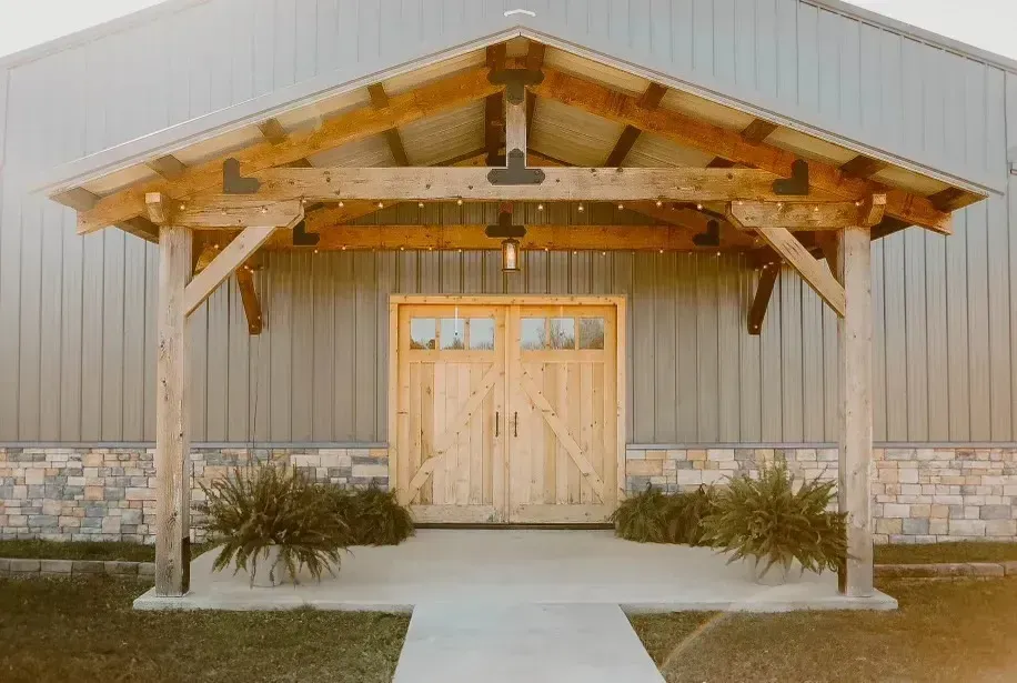 Front entrance of a rustic building with wooden double doors, stone base, and covered porch