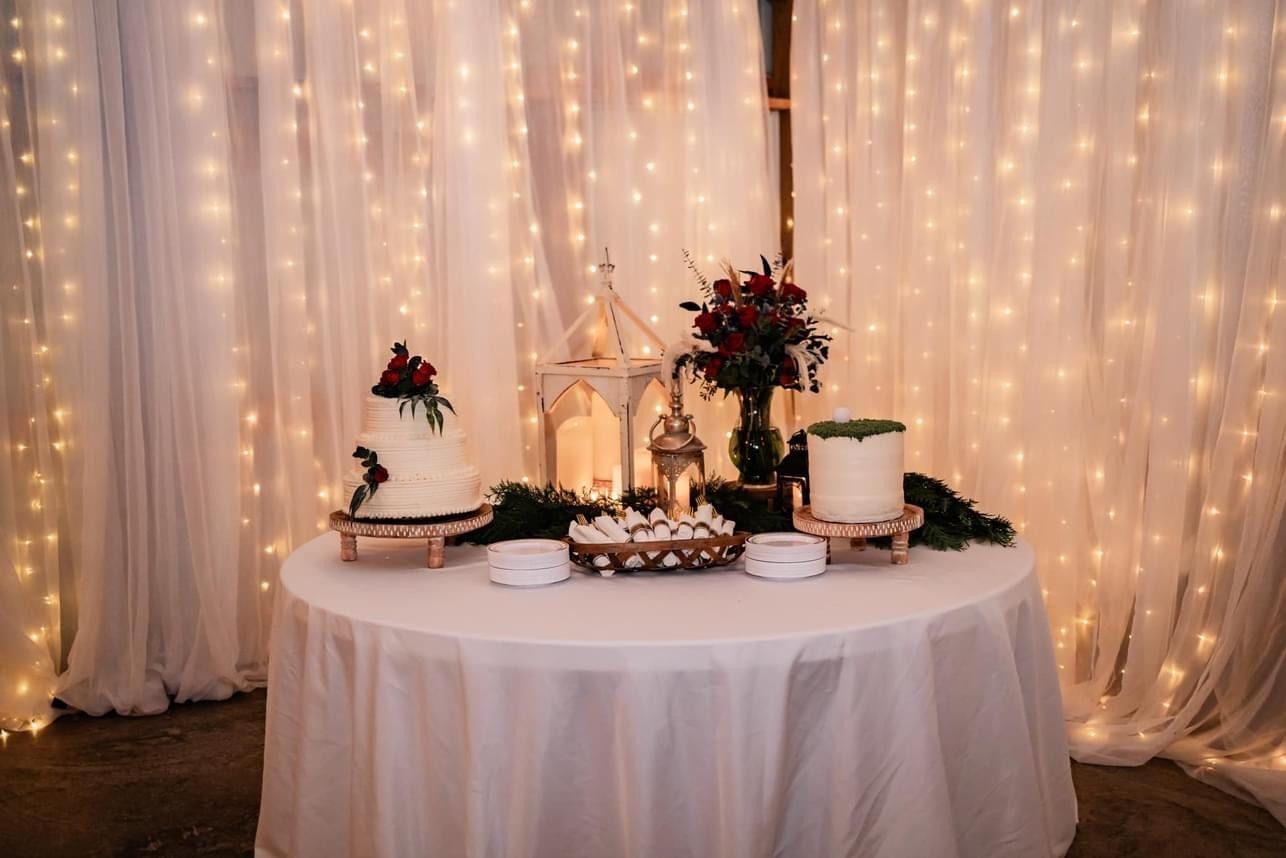 Decorated round table with flowers and cakes before warm string-light drapes