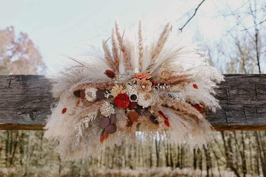 Boho dried floral arrangement with pampas grass and orange blooms on a rustic wooden fence outdoors