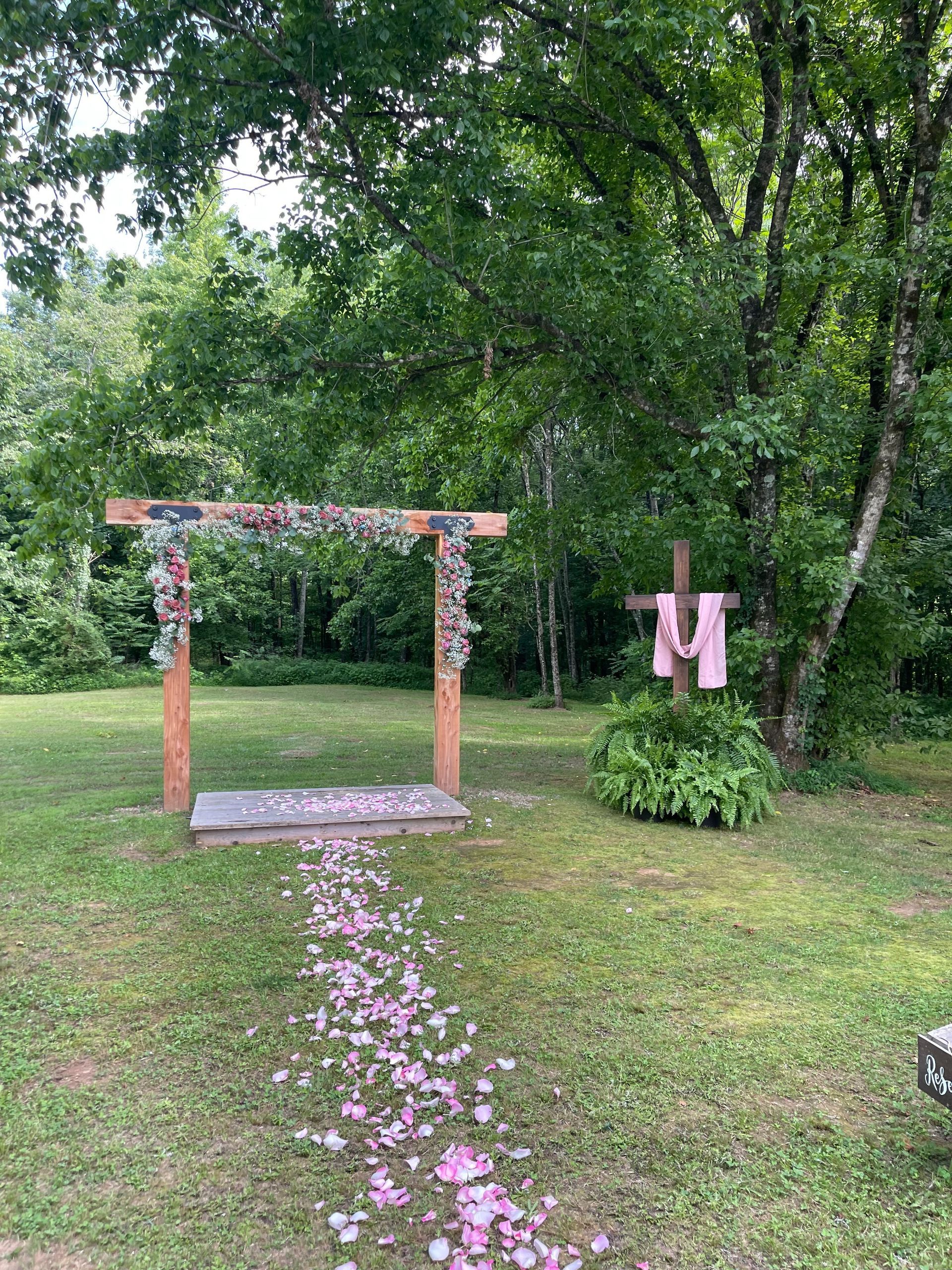 Flower-decorated wooden arch on a lawn with pink petals leading through a green garden