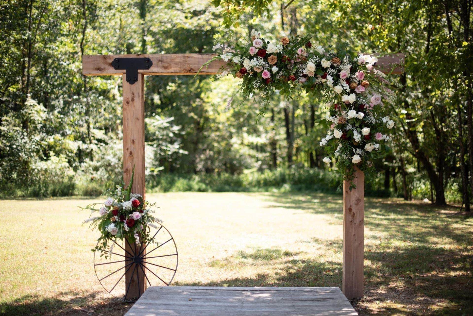 Rustic wooden wedding arch decorated with white and pink flowers in a wooded outdoor setting