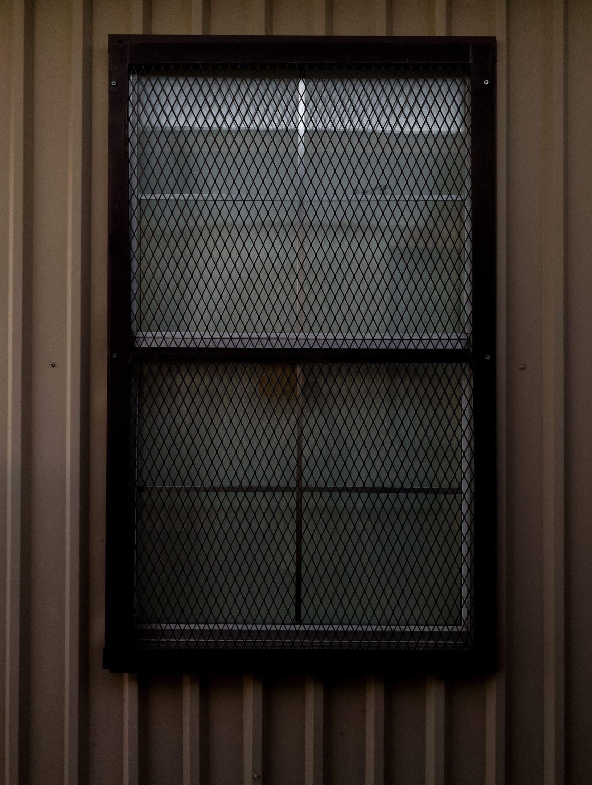 Small dark-framed window with a mesh screen on a brown corrugated wall.