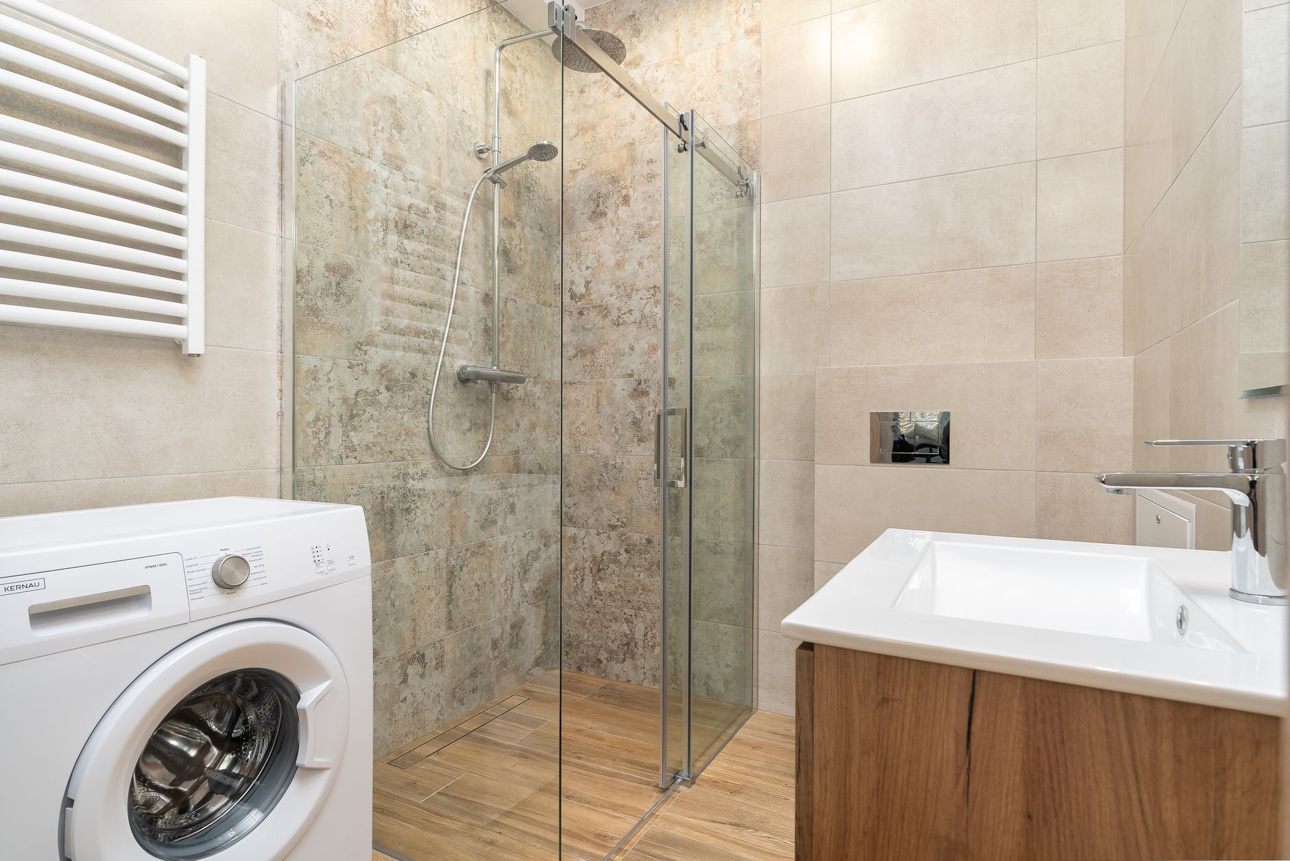 Modern bathroom with a glass shower, sink, and a washing machine.