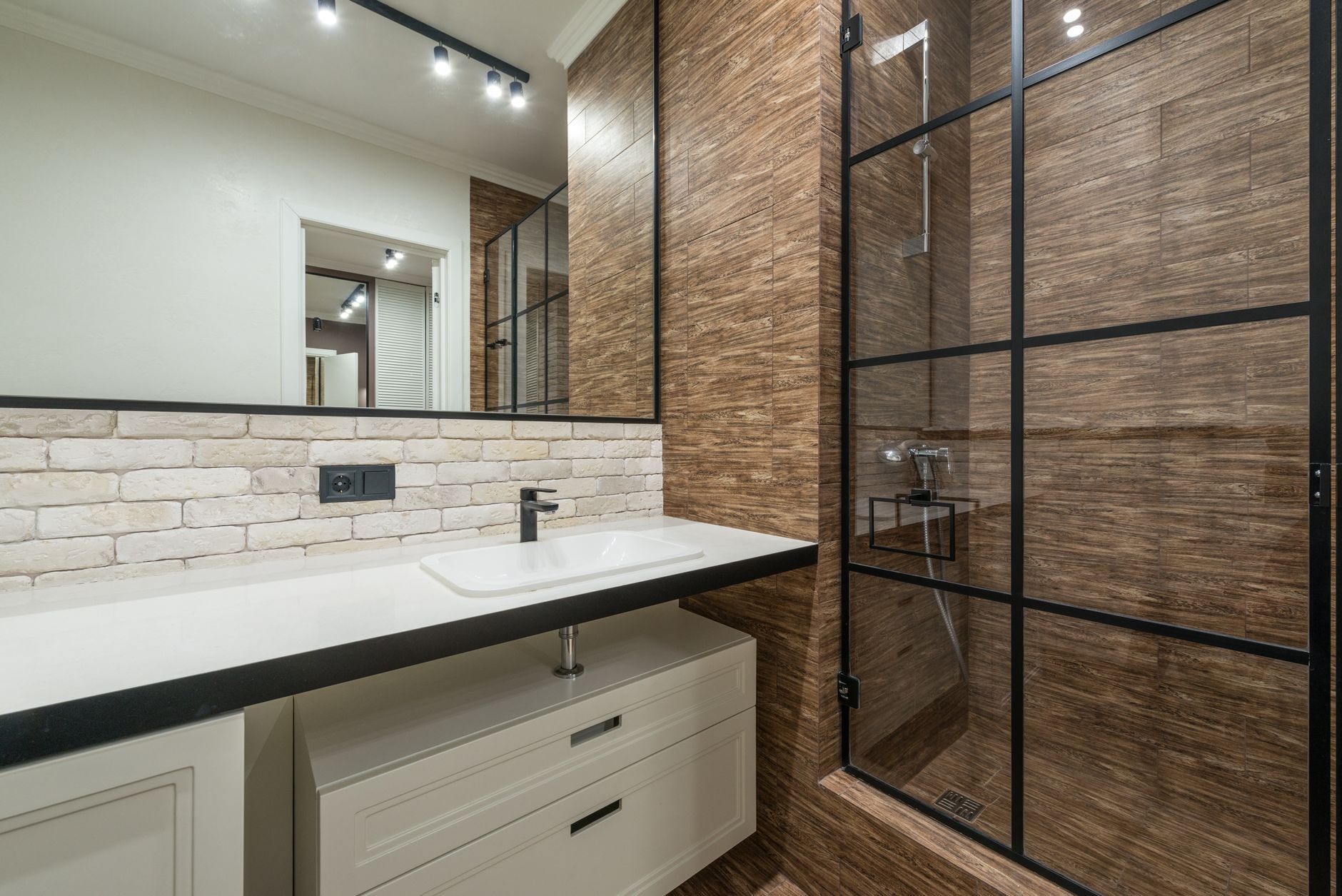 Modern bathroom with white vanity, marble countertop, brick backsplash, and black-framed glass shower door