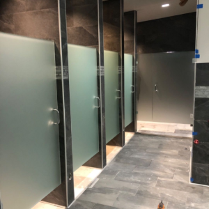Modern restroom stall area with frosted glass doors and dark tile flooring