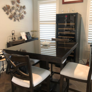 Dining room with dark wood table, chairs, and black cabinet beside windows with white blinds.