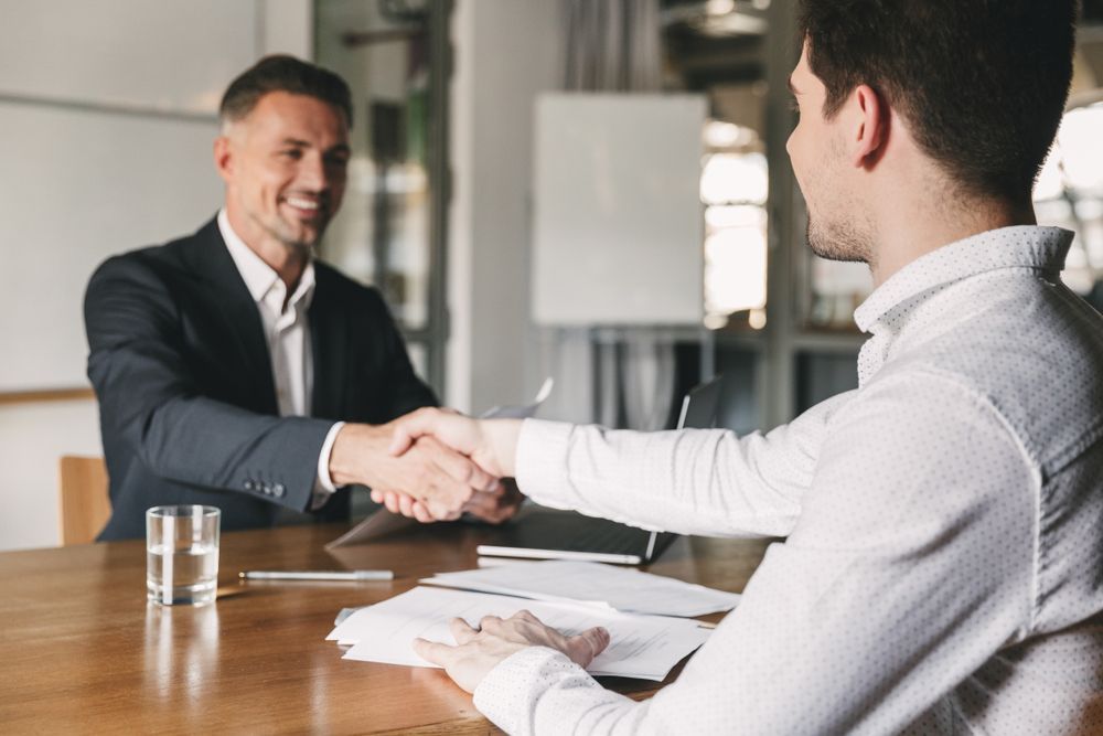 Two Men Are Shaking Hands Over Some Paper — Michael Andrews Taxation & Accounting Services In Pacific Paradise, QLD