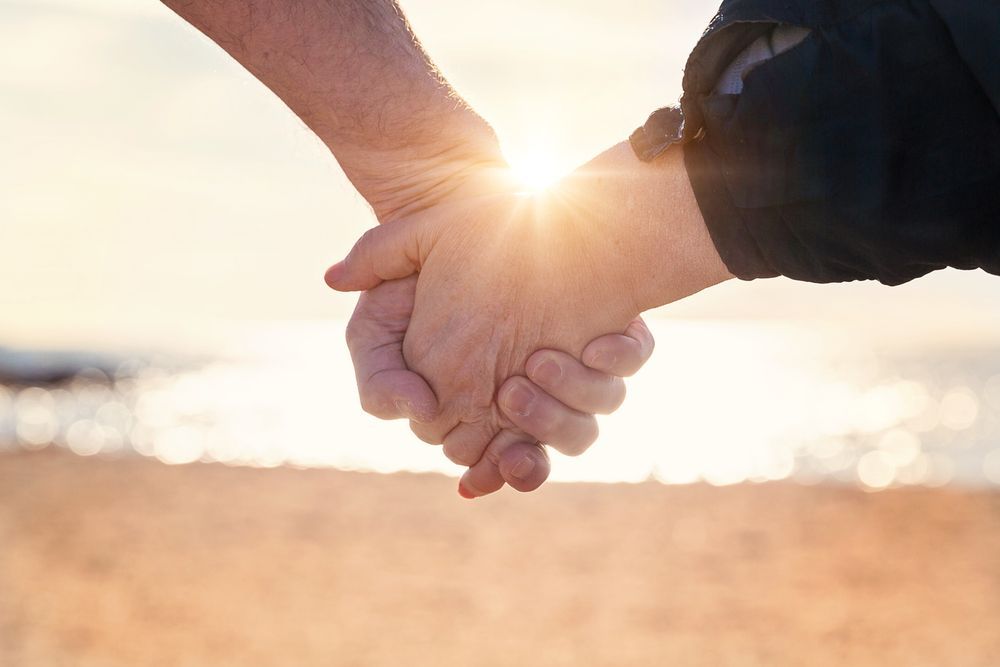Couple Holding Hands At The Beach With The Sun In Front Of Them — Michael Andrews Taxation & Accounting Services In Pacific Paradise, QLD