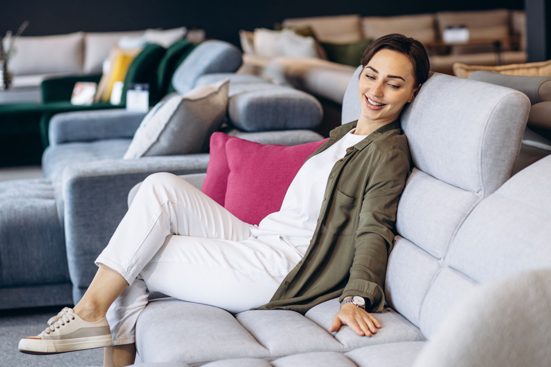 Smiling woman relaxing on a light gray sofa in a furniture showroom.