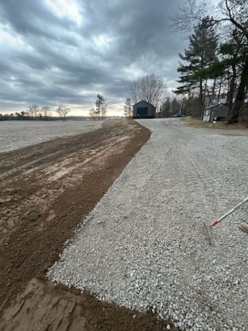 New gravel driveway levelled with excavator, leading to a large shop.