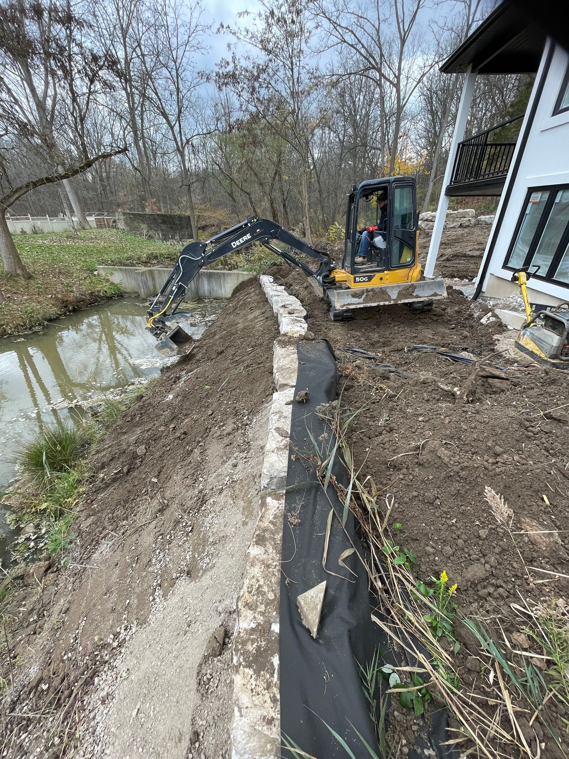 Mini excavator digging and clearing a ditch. Landscaping beside newly built house.