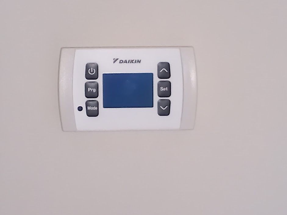 Termostato Daikin bianco su una parete chiara con pulsanti e display blu.